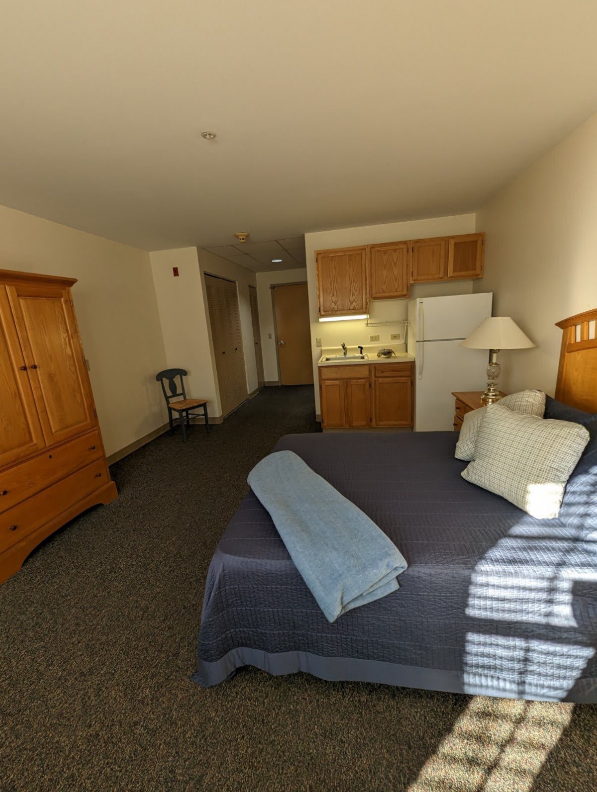 A cozy hotel room with a kitchenette, featuring a neatly made bed and wooden furniture.
