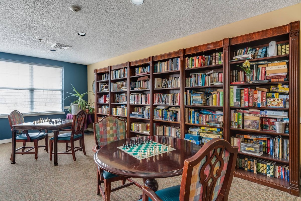 A cozy library room with bookshelves and game tables, featuring a chessboard setup.