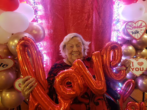 A joyful celebration of love with vibrant decorations and a smiling elder holding 'love' balloons.