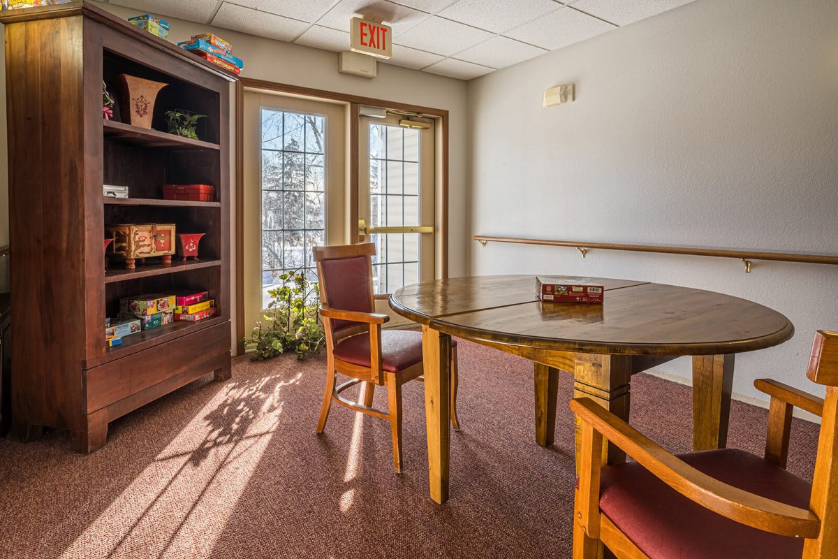 A cozy office meeting room with a wooden table, chairs, and a bookshelf by the window.