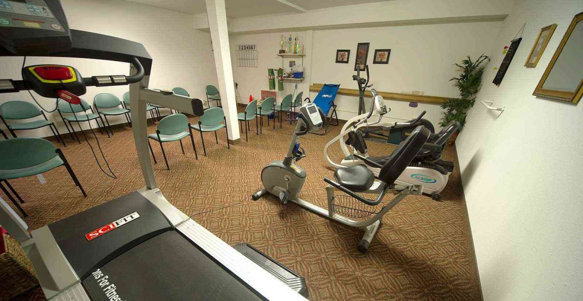 A small gym room with exercise equipment and chairs arranged along the walls.
