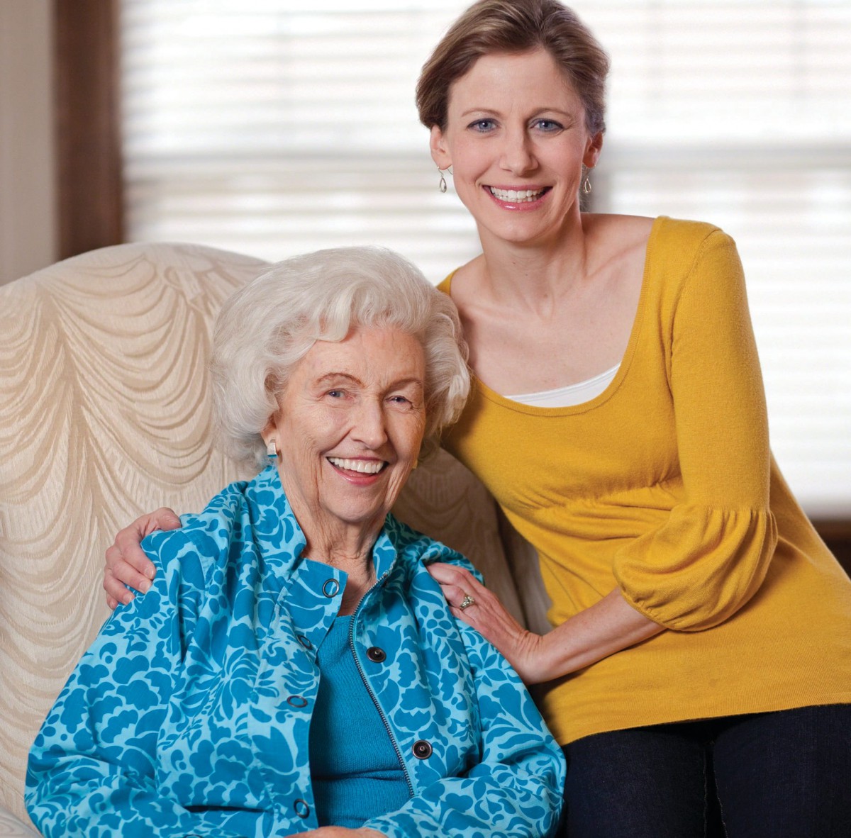 A younger woman and an elderly woman smiling together indoors.