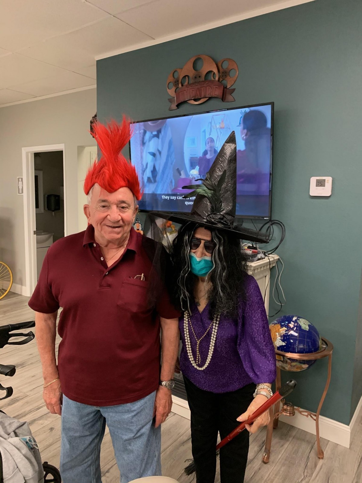 Two people dressed in Halloween costumes, one wearing a red wig and the other in a witch hat with a mask.
