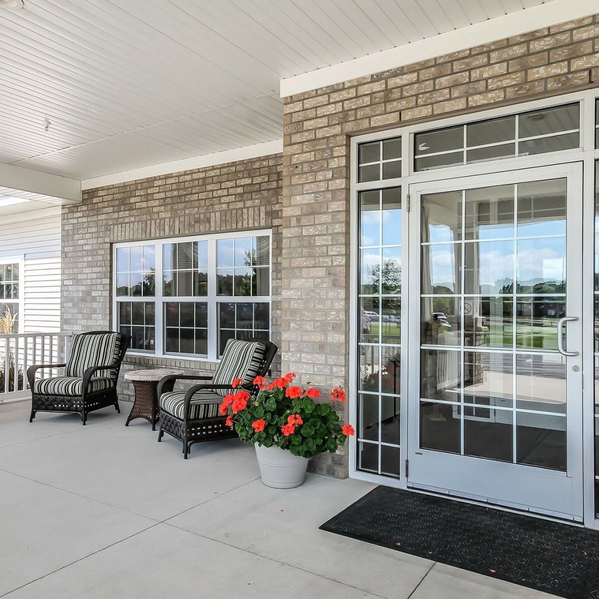 A cozy porch with brick walls, featuring outdoor seating and a flower pot next to glass doors.
