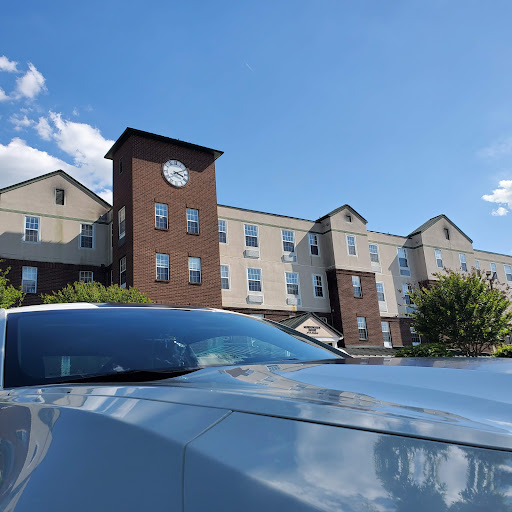 A modern hotel with a clock tower, featuring a sleek car in the foreground under a clear blue sky.