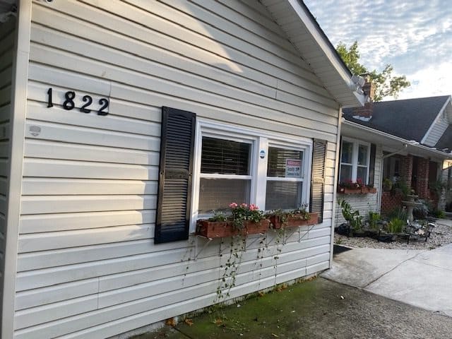 A quaint house exterior featuring white siding, black shutters, and a flower box below the windows.