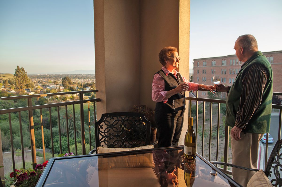 Two people enjoying wine and conversation on a balcony at sunset.