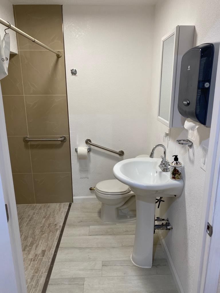 A clean, accessible bathroom with a sink and toilet featuring handrails, tiled flooring, and white walls.