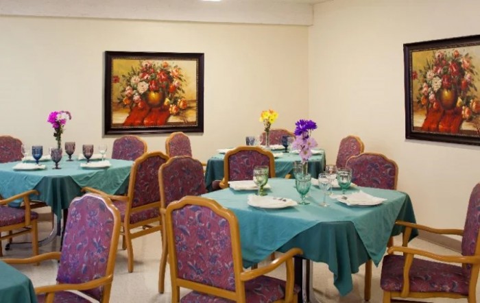 A cozy dining room with tables set for a meal, featuring teal tablecloths and floral decor.