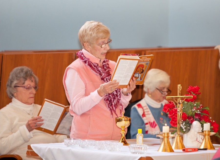 A group of people participating in a church service, with one person reading from a book.