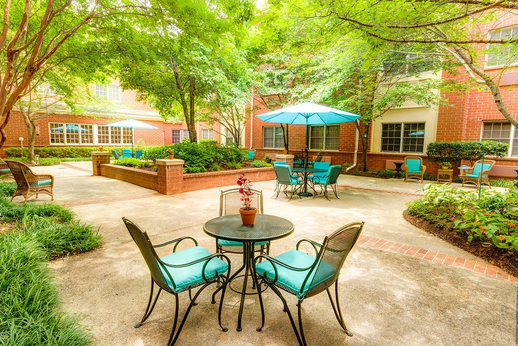 A serene patio area with tables, chairs, and umbrellas surrounded by lush greenery.