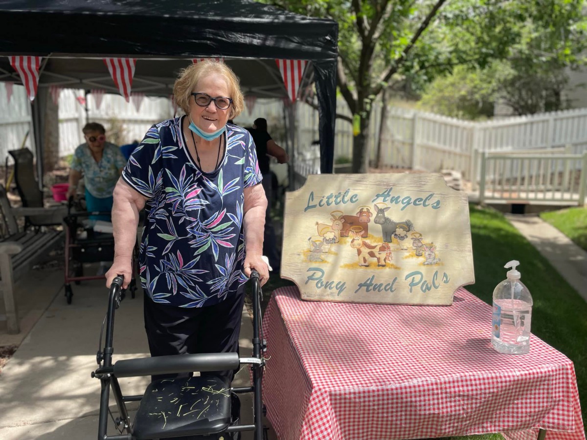 An elderly woman with a walker stands next to a sign at an outdoor gathering.