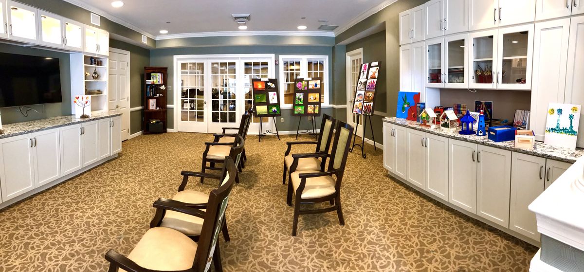 An indoor art exhibition with paintings displayed on easels and chairs arranged for viewing.
