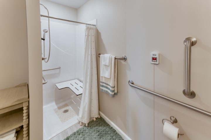 An accessible bathroom with safety features including handrails and a shower seat.