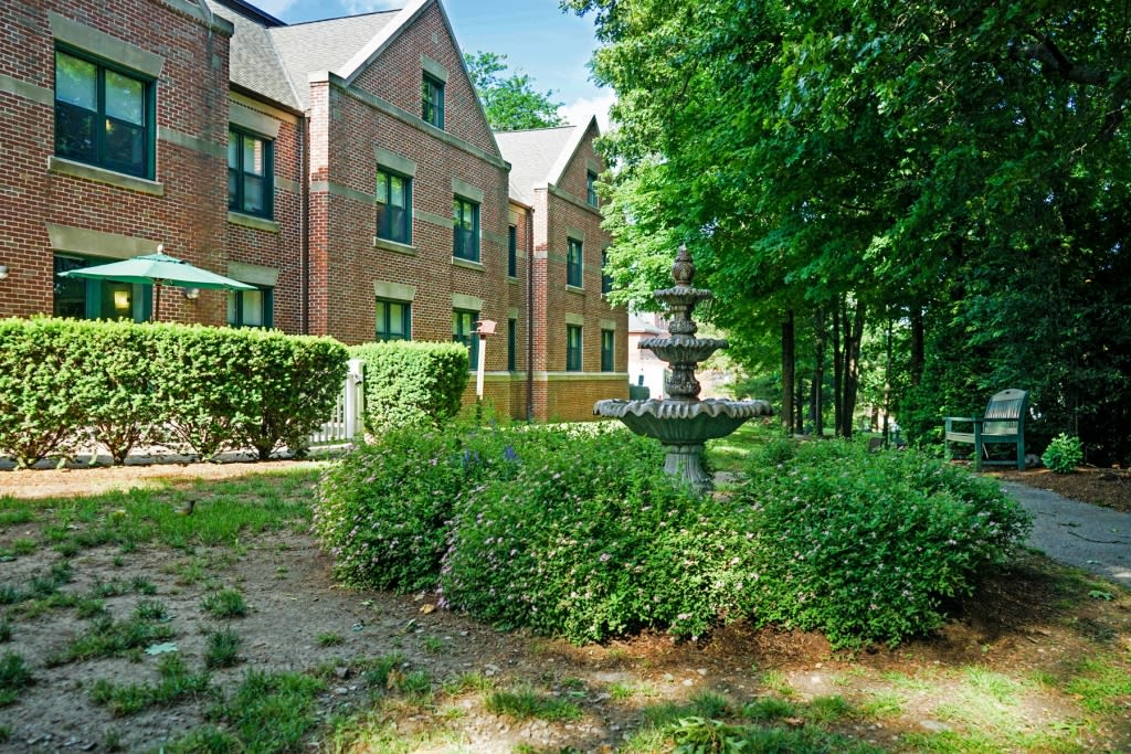 A brick building surrounded by lush greenery and a decorative fountain.