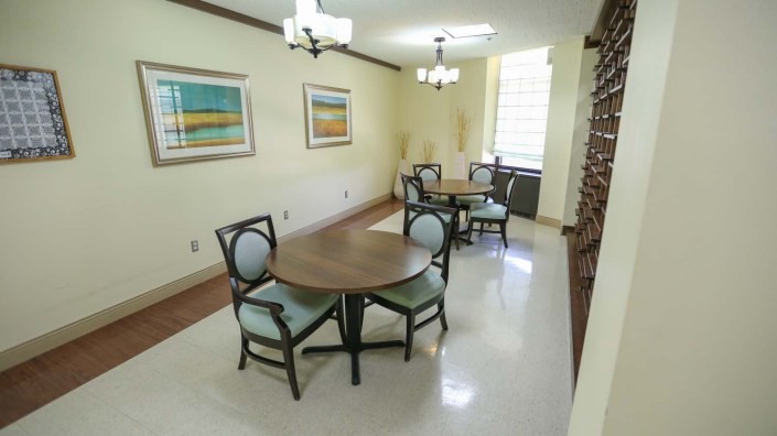 A dining room with several round tables, chairs, and wall artwork, illuminated by ceiling lights.