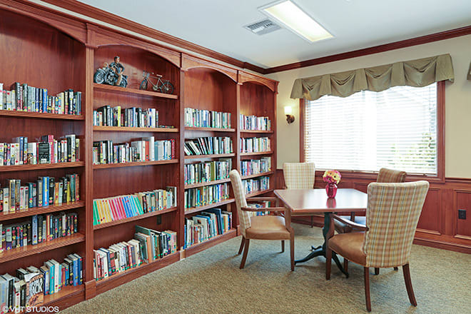 A cozy reading area with bookshelves and a table surrounded by chairs next to a window.