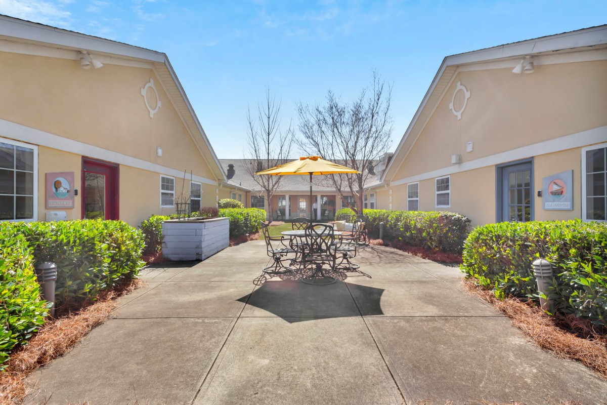 A sunny courtyard with outdoor seating and an umbrella between two buildings.