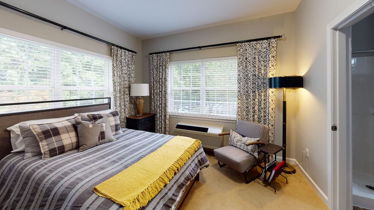 A cozy bedroom featuring a striped bed with a yellow blanket, patterned curtains, and comfortable seating.
