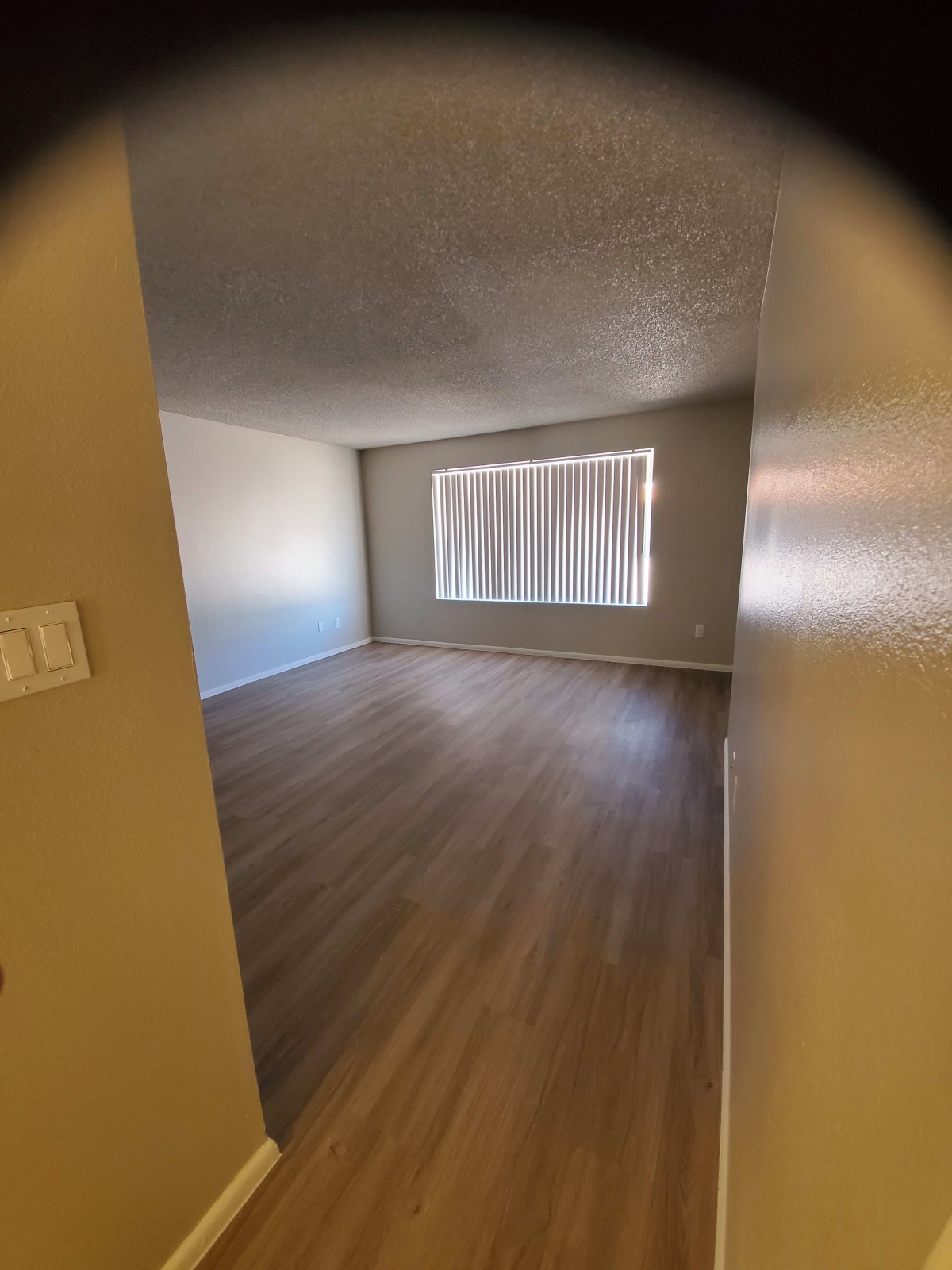 An empty room with wooden flooring and a window covered by curtains.