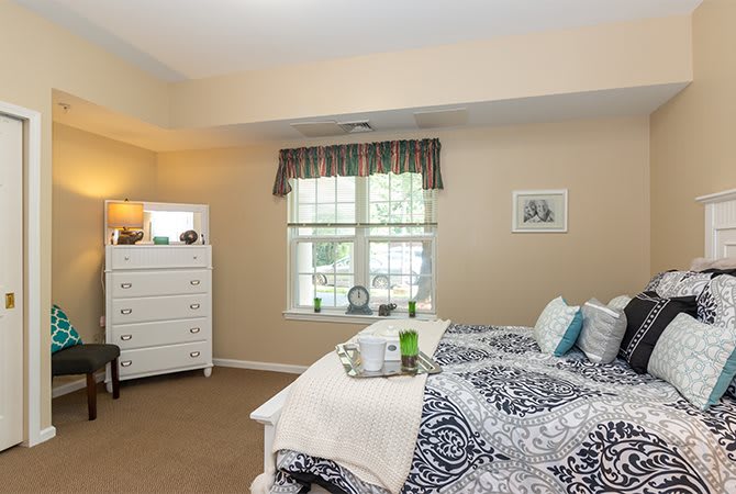 A cozy bedroom featuring a bed with patterned bedding, a white dresser, and a window with curtains.