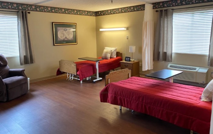 A well-organized bedroom with two beds, each covered with red bedspreads. The room features wooden flooring, curtains on the windows, and a decorative frame on the wall.
