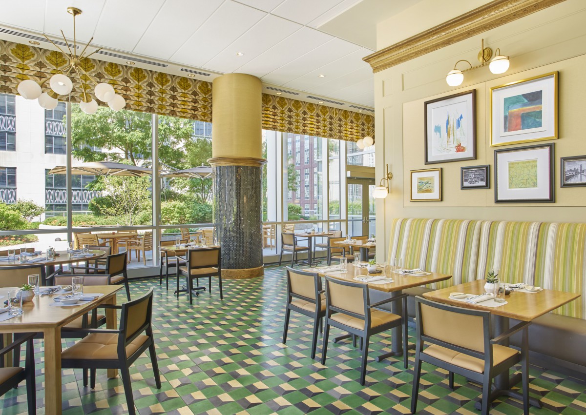 A bright and spacious restaurant interior with large windows, decorative artwork, and neatly arranged tables and chairs.