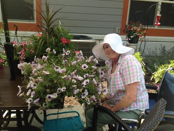A person in a white hat sits next to a blooming flower arrangement outdoors.