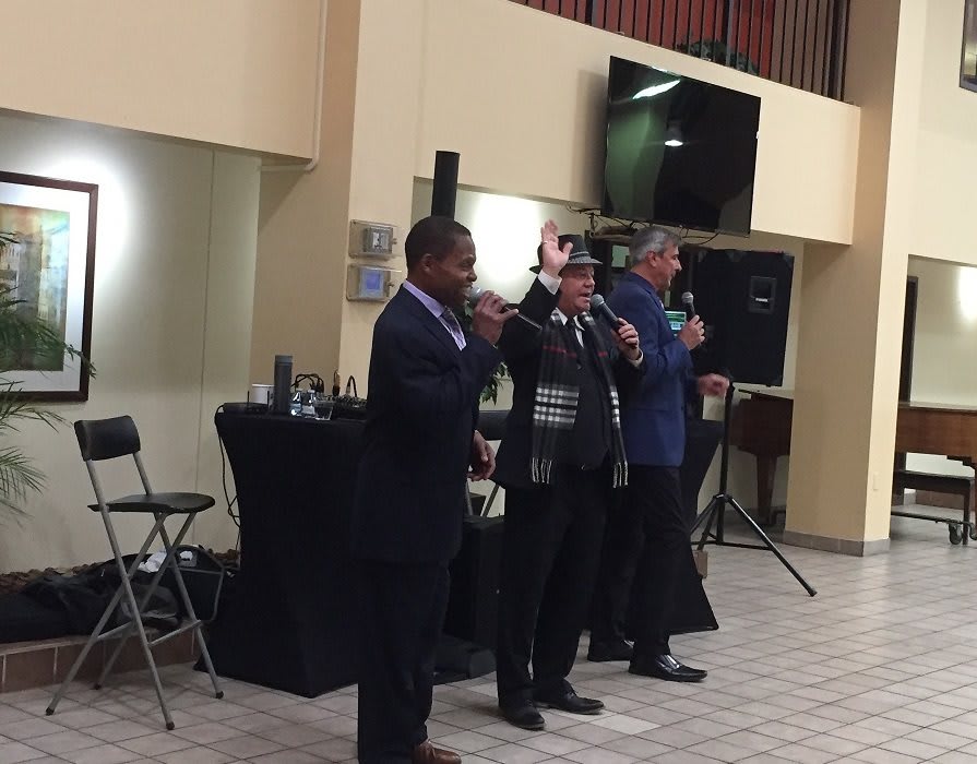 Three individuals speaking at an indoor event with microphones.