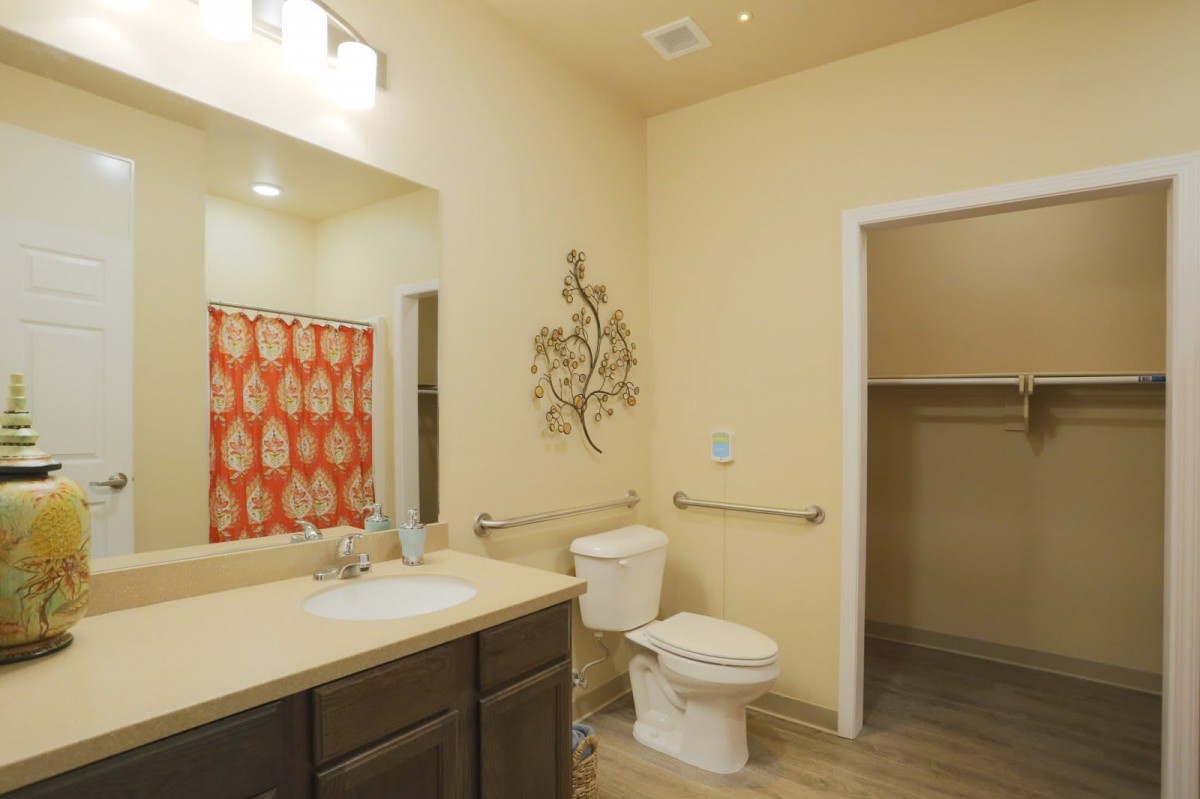 A well-lit bathroom featuring a sink, toilet, mirror, and a stylish orange shower curtain.