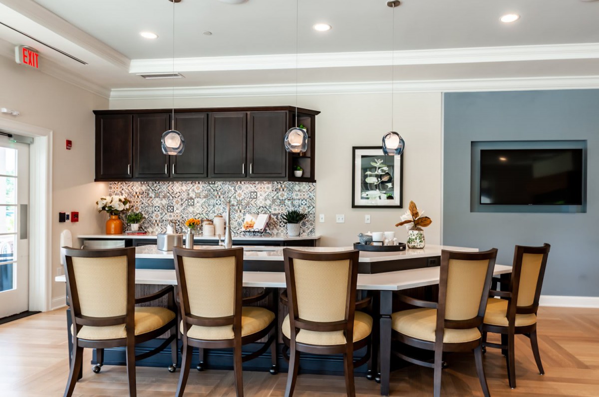 A modern kitchen interior with a long counter and bar stools, illuminated by stylish pendant lights.