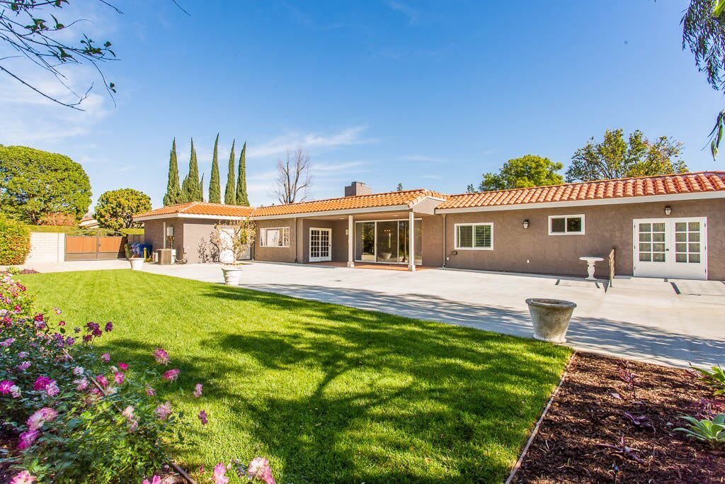 A beautiful backyard view of a single-story house with a well-maintained lawn and garden.