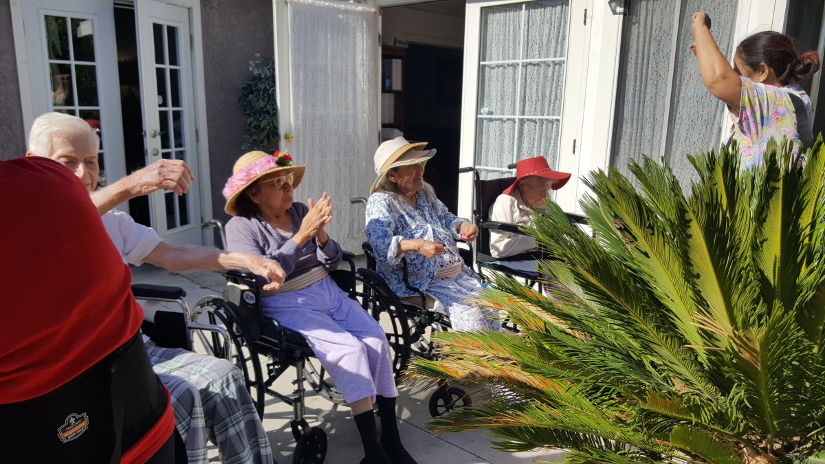 A group of elderly women sitting in wheelchairs, enjoying a sunny day outdoors on a patio.