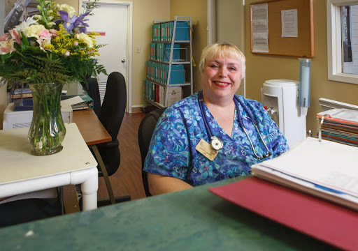 A friendly receptionist smiles at the camera in a welcoming office environment.