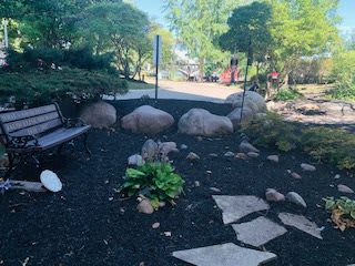 A serene garden landscape featuring a bench, pathway, and lush greenery.