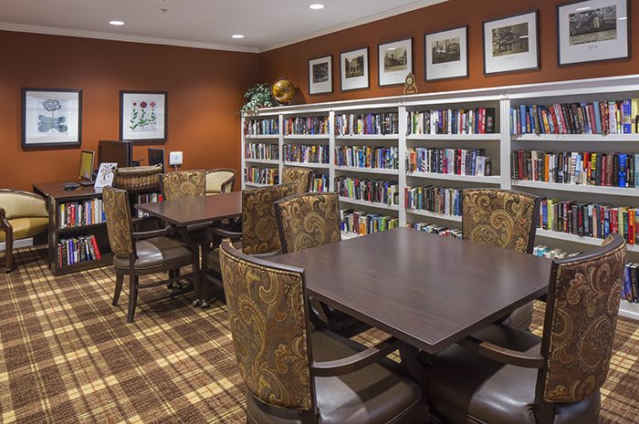 A cozy library space with bookshelves, tables, and chairs for reading.
