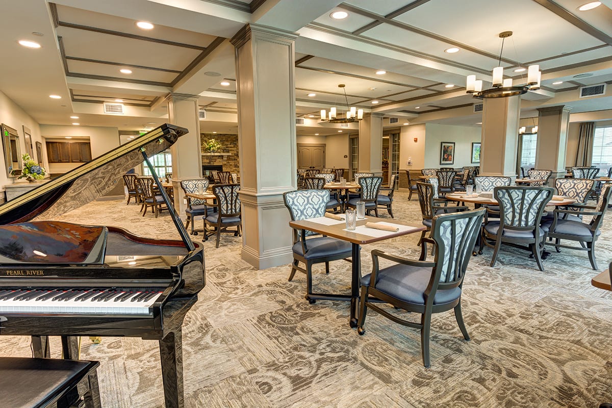 A spacious dining area featuring elegant decor, complete with a grand piano and neatly arranged tables and chairs.