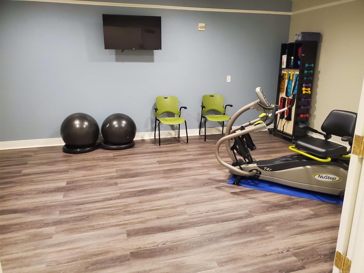 A small gym area featuring a treadmill, exercise balls, chairs, and a television on the wall.