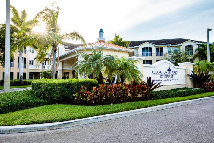 A picturesque view of a building surrounded by lush greenery and palm trees, with sunlight streaming down.