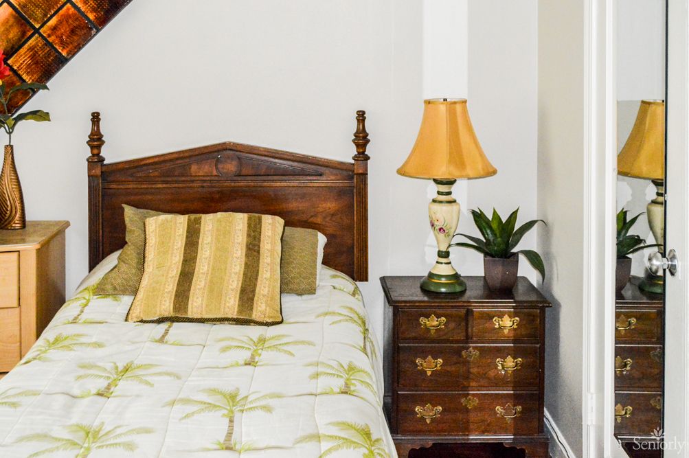A cozy bedroom with a wooden bed and nightstand featuring a lamp and plant.