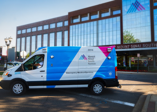 A healthcare ambulance parked on a city street in front of a modern building.