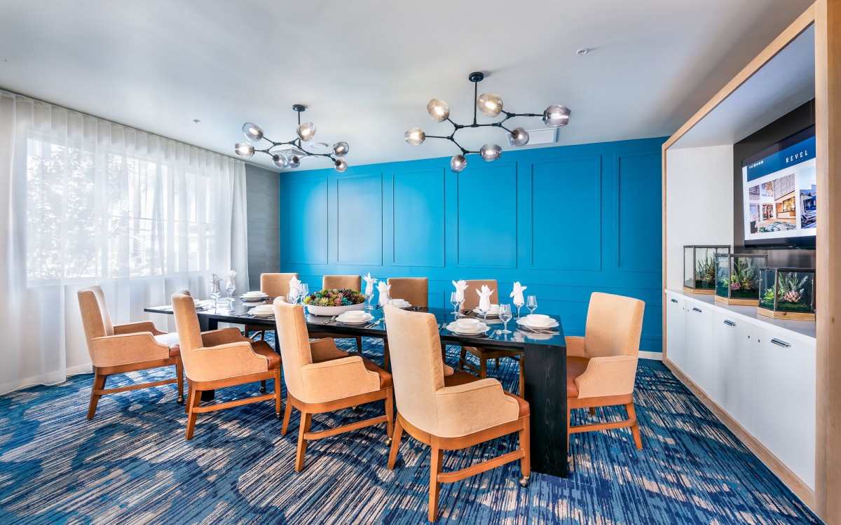 A modern conference room with blue walls, elegant chandeliers, and comfortable seating around a large table.