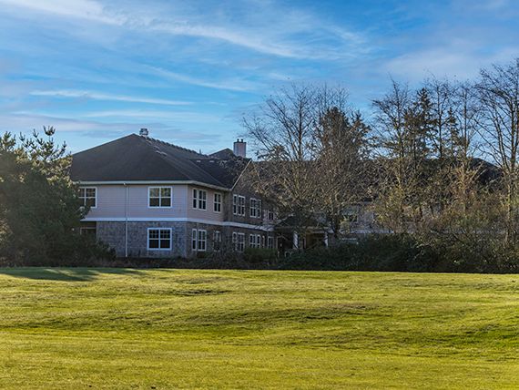 A suburban house with a large lawn and trees under a blue sky.