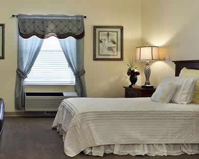 A cozy bedroom with a neatly made bed, decorative lamp, and window with curtains.