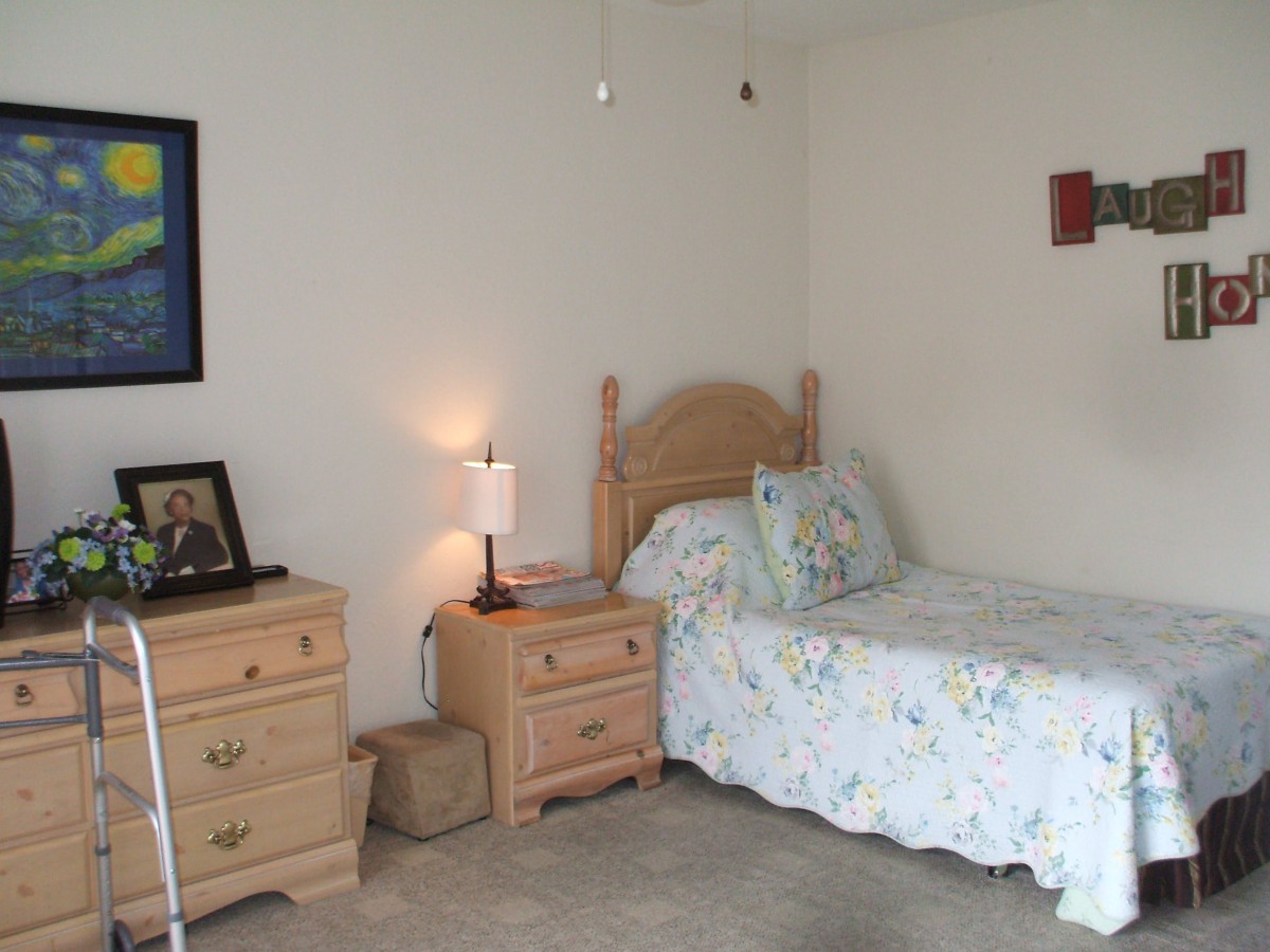 A cozy bedroom featuring a single bed with floral bedding, a nightstand with a lamp, and framed artwork on the wall.