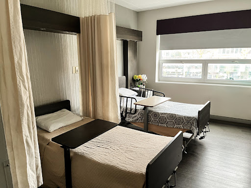 A modern patient room in a hospital, featuring two beds separated by curtains and plenty of natural light.