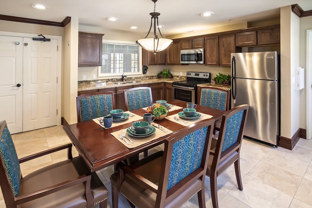 A modern kitchen and dining area with a wooden table set for four, featuring stainless steel appliances and wood cabinetry.