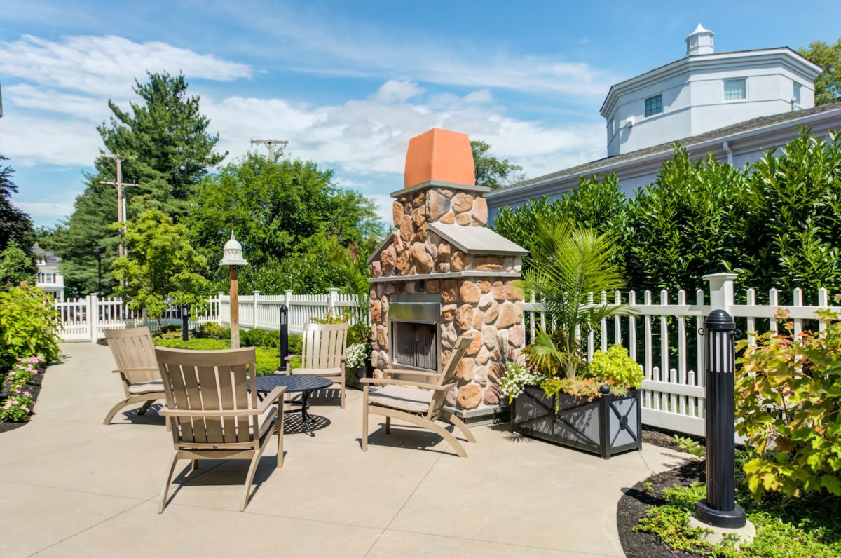 A cozy outdoor patio featuring a stone fireplace surrounded by garden furniture and lush greenery.