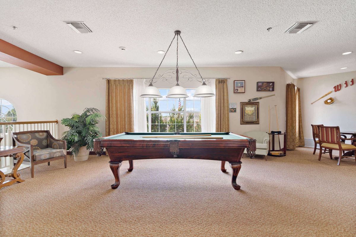 A spacious game room featuring a classic pool table and a hanging light fixture, with large windows and elegant curtains.