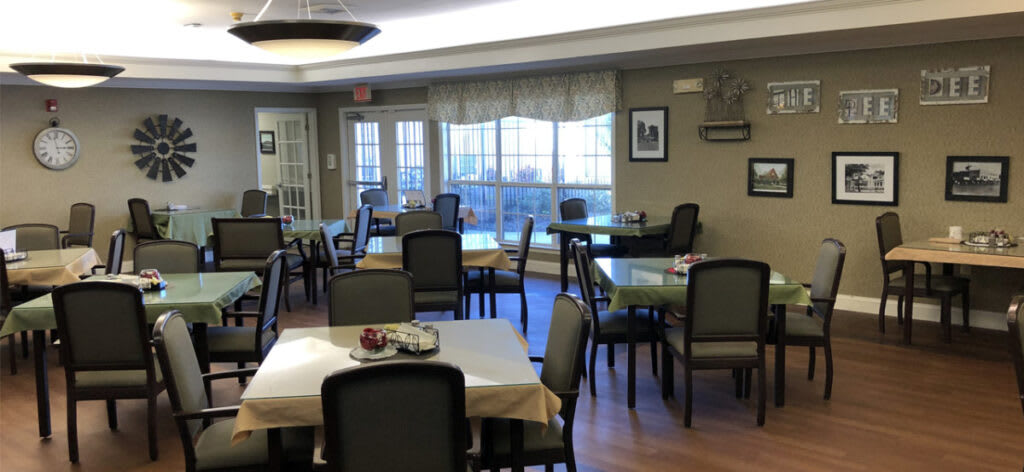A neatly arranged dining room with multiple tables and chairs by large windows.